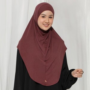May include: A burgundy hijab, a head covering worn by some Muslim women, is draped over the head and shoulders. The hijab is made of a soft, flowing fabric. The person in the image is wearing a black top.
