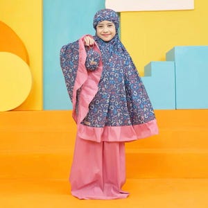 May include: A young girl wearing a prayer outfit. The outfit includes a head covering, a long cape, and matching pants. The fabric is patterned with colorful numbers and symbols on a dark blue background, with pink accents.