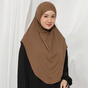 May include: A brown hijab, a head covering worn by some Muslim women. The hijab is made of a soft, draping fabric and covers the head and neck. The woman in the image is wearing a black top.