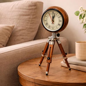 May include: A vintage clock with a wooden casing and a white face with Roman numerals. The clock is mounted on a wooden tripod stand with silver metal details. The clock is on a wooden table.