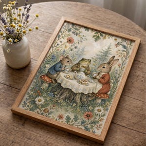 May include: A framed print depicts a whimsical tea party scene. A mouse, frog, and rabbit are gathered around a table set on a tree stump, enjoying tea and treats. The artwork features a light wood frame and a floral and forest background.