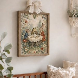 May include: A framed print depicts a whimsical tea party scene with a mouse, frog, and rabbit seated around a table. The artwork features a rustic wooden frame, a cream-colored lace bow, and a floral and forest background. The characters are dressed in vintage clothing.