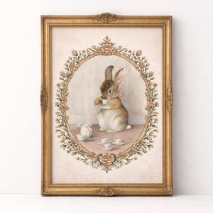 May include: A framed print featuring a watercolor illustration of a rabbit enjoying tea. The rabbit is wearing a pink bow and is surrounded by teacups and a floral border. The frame is gold-colored.