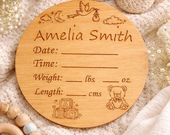 Puede incluir: Un letrero de madera para anunciar el nacimiento de un bebé con el nombre "Amelia Smith" grabado. Incluye espacios para la fecha, hora, peso (lbs, oz) y longitud (cm). Con un oso de peluche, bloques ABC y una cigüeña.