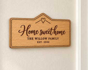 Puede incluir: Un letrero rectangular de madera marrón claro con un borde superior en punta. El letrero presenta un icono de corazón grabado con láser y el texto "Home sweet home", "THE WILLOW FAMILY" y "EST. 2026" en letras marrón oscuro con borde.