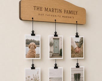 Puede incluir: Un expositor de pared de madera marrón claro con el texto THE MARTIN FAMILY y OUR FAVOURITE MOMENTS. Tiene tres cuerdas negras que cuelgan de la madera, cada una con dos impresiones fotográficas verticales sujetas por clips de metal negro.