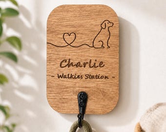 Puede incluir: Soporte de correa para perros de madera con un gancho negro. El soporte está grabado con la silueta de un perro, un corazón y el nombre "Charlie" encima de "- Walkies Station -". Una correa verde y marrón cuelga del gancho.