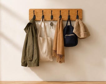 Puede incluir: Un perchero de pared rectangular de madera clara con seis ganchos de metal negro que sostiene una chaqueta verde oliva, una bolsa de tela beige, un juego de llaves, una bufanda color canela, una mochila azul marino y un gorro de punto sobre un banco.