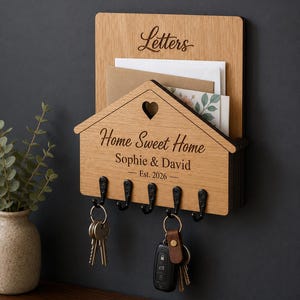 Puede incluir: Un organizador de correo y llavero de pared de madera clara. La secci&oacute;n superior tiene la palabra Letters. La parte frontal con forma de casa presenta un recorte de coraz&oacute;n, el texto Home Sweet Home, Sophie & David, y Est. 2026, con cinco ganchos.