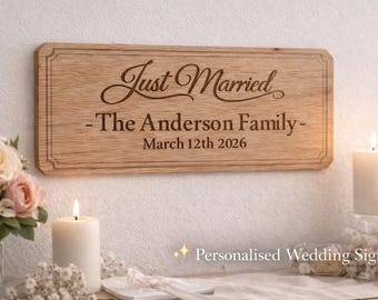 Puede incluir: Un letrero rectangular de madera con las palabras "Just Married" y "- The Anderson Family - March 12th 2026" grabadas. El letrero se muestra en una pared, con velas y flores en primer plano.