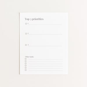 May include: A white notepad with the text "Top 3 priorities" at the top, followed by three numbered lines with checkboxes. Below, the text "Other tasks" is followed by a series of checkboxes and lines. The notepad is on a white background.