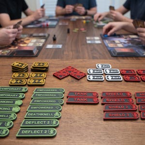 May include: A collection of rectangular and diamond-shaped game tokens in yellow, red, white, and green. The tokens feature text including "BUFF," "STUNNED," "TANK," "SHIELD," "ASSAULT," "TEMPORARY," "EMPOWERED," "GANKING," "DEATHKNELL," and "DEFLECT."