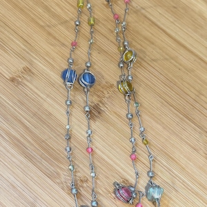 May include: A long silver-tone chain necklace featuring multiple round beads in various colors including blue, yellow, pink, green, and clear. The beads are encased in thin silver wire cages and interspersed with small silver-tone metal spacer beads.