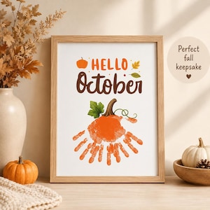 Może przedstawiać: Oprawiony wydruk artystyczny z napisem Hello October w kolorze pomarańczowym i brązowym. Projekt zawiera małą ikonę pomarańczowej dyni, dwa jesienne liście oraz duży pomarańczowy odcisk dłoni w kształcie dyni z zieloną łodygą.