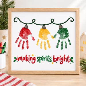 May include: A square framed print featuring a string of dark green Christmas lights with three handprints hanging as bulbs in red, yellow, and green. Below the handprints, the text reads "making spirits bright" in red and green script.