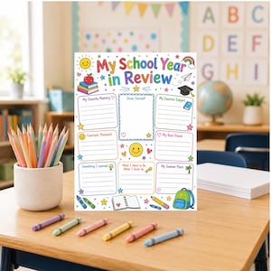 May include: A colorful "My School Year in Review" poster with spaces for memories, drawings, and plans. The poster is decorated with a sun, rainbow, and school-themed illustrations. Crayons and pencils are on the wooden desk.