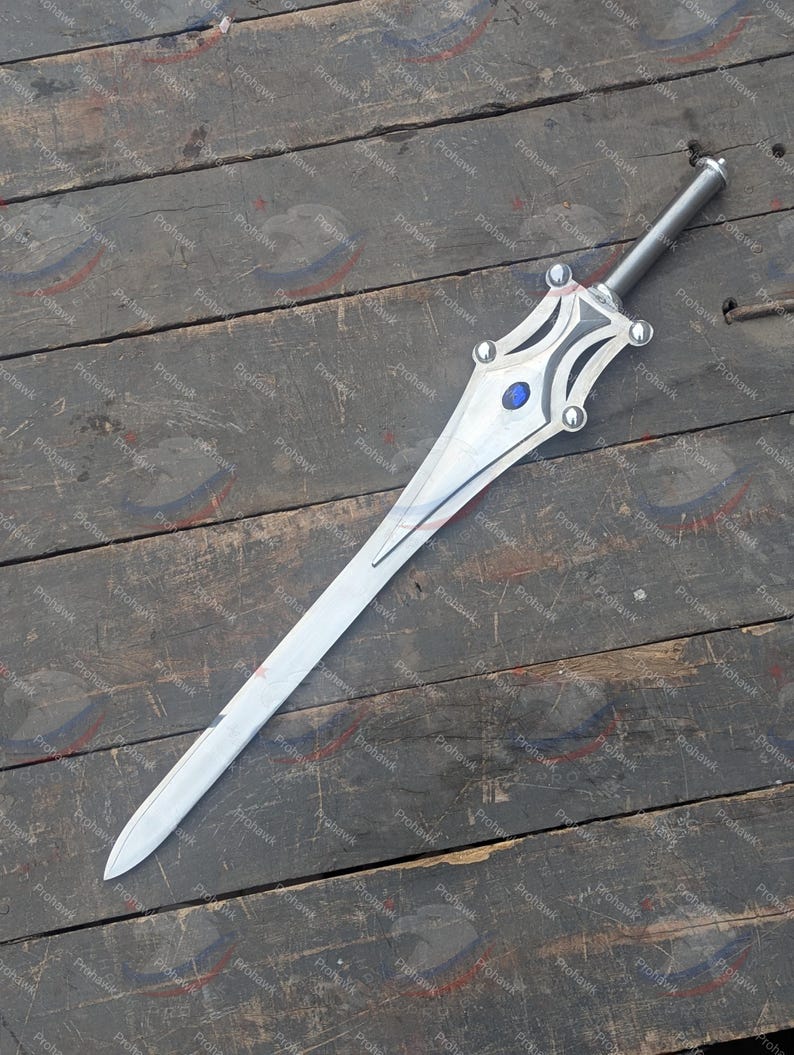 May include: A silver sword with a long, pointed blade and a decorative hilt. The hilt features a blue gem and silver accents. The sword is displayed on a weathered wooden surface.