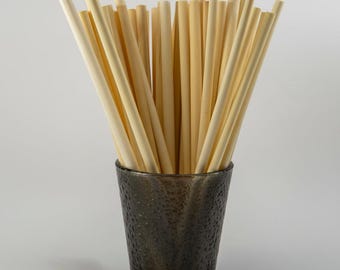 May include: A collection of light beige bamboo straws in a dark grey textured glass. The straws are cylindrical and vary slightly in colour. The glass has a speckled appearance. The straws are arranged vertically, filling the glass.