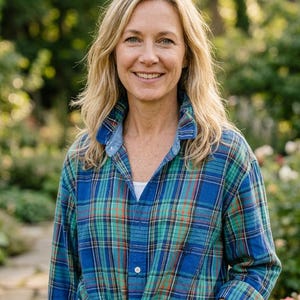 Puede incluir: Una mujer con una camisa a cuadros azul, verde y naranja atada a la cintura. La camisa tiene cuello abotonado y se combina con vaqueros azules. El fondo presenta un jardín con vegetación y un camino de piedra.