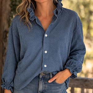 May include: A blue button-down shirt with white polka dots. The shirt has a ruffled collar and cuffs, and is paired with blue jeans. The model is wearing the shirt and jeans.