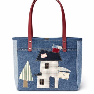May include: Denim tote bag with red handles. The bag features a patchwork design of a house, tree, and other elements. The house has a checkered pattern and a chimney. The bag is made of denim.
