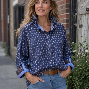 Op de afbeelding: Een marineblauw overhemd met een klein bloemenpatroon, gecombineerd met lichtblauwe jeans en een bruine leren riem. Het overhemd heeft een gerimpelde kraag en opgerolde mouwen met een patroonmanchet.