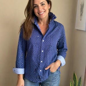 Puede incluir: Una camisa azul con un patrón circular blanco. Tiene botones y mangas largas, con los puños doblados. Se combina con unos vaqueros azules.