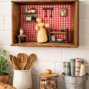May include: A wooden shadow box with a miniature kitchen scene, featuring a red and white checkered backdrop. The scene includes a doll figure, shelves with tiny items, and a small table. Kitchen utensils, bread, and tomatoes are in the foreground.