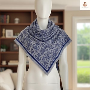 Pode incluir: Lenço azul e branco estampado, exibido em um manequim. O lenço tem um design repetitivo e uma borda com franjas. O lenço é drapeado ao redor do pescoço e dos ombros do manequim.