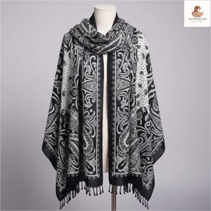 Może przedstawiać: Czarno-biała chusta w paisley z frędzlami. Chusta jest narzucona na manekina, prezentując skomplikowany wzór. Wzór zawiera mieszankę wzorów paisley i w kropki.