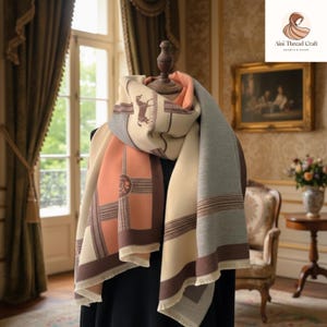 May include: A beige, peach, and grey scarf featuring a horse and rider design. The scarf has a geometric pattern with brown borders and fringe. The scarf is draped over a mannequin in a well-lit room.