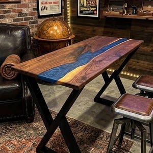 May include: A rectangular table featuring a natural dark brown wood slab with a central blue resin river inlay. The table is supported by a black metal X-shaped frame base. The wood grain is visible throughout the surface, and the blue resin has a swirling, translucent appearance that runs diagonally across the tabletop.