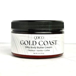 May include: A jar of QDCO Gold Coast Silky Body Butter Cream. The jar is brown with a black lid. The label is white with black text that reads "Gold Coast" and lists the scents: Coconut, Vanilla, and Coffee. Net Wt. 4 oz (113 g).