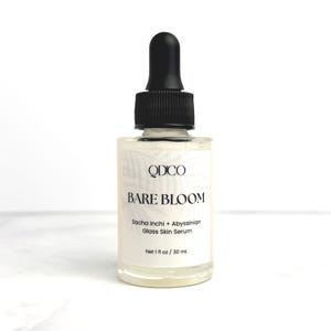 K&ouml;nnte beinhalten: Eine klare Glas-Serumflasche mit schwarzem Tropfaufsatz. Das Etikett lautet "QDCO BARE BLOOM Sacha Inchi + Abyssinian Glass Skin Serum Net 1 fl oz / 30 ml."