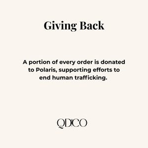 May include: Cream-colored graphic with the text "Giving Back" in a bold, black font. Below, it states that a portion of every order is donated to Polaris to end human trafficking. The logo "QDCO" is at the bottom.