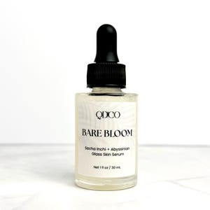 K&ouml;nnte beinhalten: Eine klare Glasflasche mit Bare Bloom Serum und einer schwarzen Pipette. Auf dem Etikett steht "QDCO BARE BLOOM Sacha Inchi + Abyssinian Glass Skin Serum". Die Flasche enth&auml;lt 30 ml Serum.