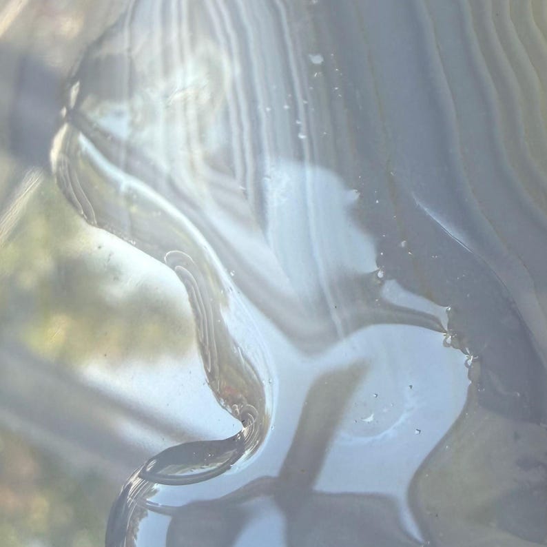 May include: Abstract close-up of a glass object with flowing, curved lines. The glass has a translucent, milky appearance with subtle variations in color, ranging from light blue to white. The image has a soft, ethereal quality.
