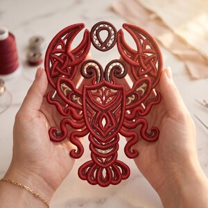 May include: A red embroidered lobster applique featuring intricate corded details and a central shield-like motif. The design incorporates swirling patterns and knot-work elements in shades of deep red and burgundy, creating a textured surface.