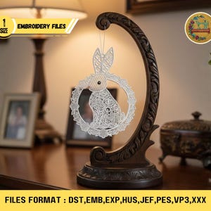 Op de afbeelding: Een decoratieve houten standaard met een donkerbruine afwerking, met een wit, lasergesneden paashaasornament. Het ornament is cirkelvormig met een konijnensilhouet. De tekst "EMBROIDERY FILES" is zichtbaar. De afbeelding toont ook de tekst "FILES FORMAT: DST, EMB, EXP, HUS, JEF, PES, VP3,XXX".