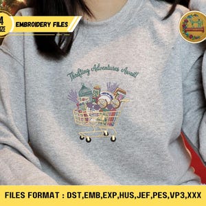 May include: A gray sweatshirt with an embroidered design of a shopping cart filled with various items. The text "Thrifting Adventures Await!" is above the cart. The image also includes text indicating embroidery file formats and sizes.