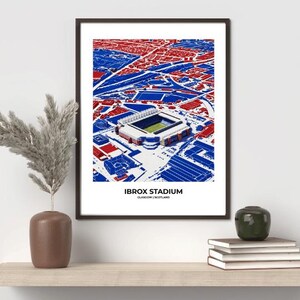 May include: Framed art print of Ibrox Stadium in Glasgow, Scotland. The artwork features a detailed aerial view of the stadium and surrounding area in red and blue. The text "IBROX STADIUM" is displayed at the bottom of the print.