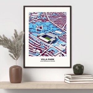 Op de afbeelding: Ingelijste kunstafdruk van Villa Park, Aston, Birmingham, Engeland. Het kunstwerk toont een luchtfoto van het stadion in tinten blauw, wit en bordeauxrood. De tekst "VILLA PARK" staat onderaan de print.