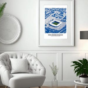 Op de afbeelding: Een ingelijste print van het King Power Stadium in Leicester, Engeland, in blauw en wit. Het kunstwerk toont een luchtfoto van het stadion en de omgeving. De tekst "KING POWER STADIUM" staat onderaan de print.