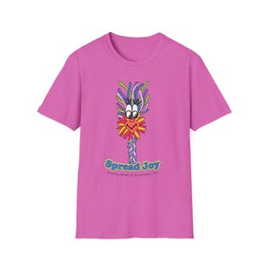 Peut inclure: Un t-shirt magenta avec un dessin d'oiseau de dessin animé coloré. L'oiseau a un bec jaune et rouge, avec une tête et un corps multicolores. Le texte "Spread Joy" est en dessous, avec "Gooney Birds of Southport, NC".