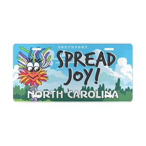 May include: A rectangular license plate with a blue sky background and white clouds. The plate features a colorful cartoon creature and the words "SPREAD JOY!" and "NORTH CAROLINA". The word "SOUTHPORT" is at the top.