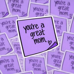 May include: A collection of purple stickers with the phrase "you're a great mom" in black script. Each sticker has a small heart symbol. The stickers are scattered across a surface.