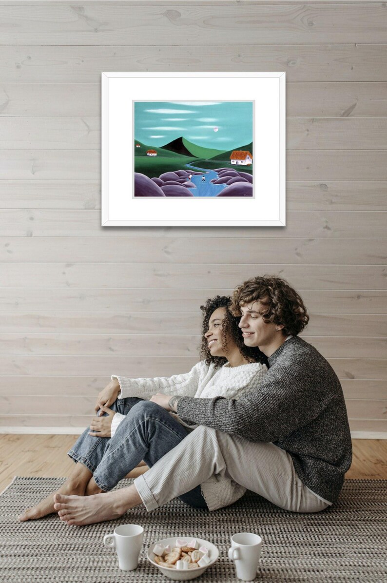 May include: A framed landscape painting featuring a winding blue river flowing through green hills, large purple boulders, and two small white houses with red roofs under a light blue sky with a pale moon and thin white clouds.