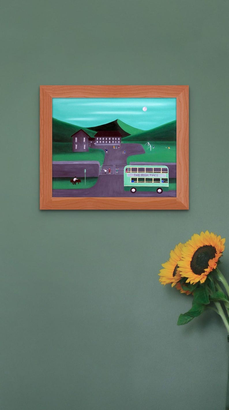 May include: A framed painting depicts a green double-decker bus labeled THE IRISH TIMES driving past a stone wall, a park with figures, and buildings set against rolling green hills under a pale moon in a light blue sky.