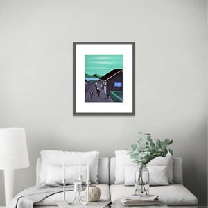 May include: A framed art print featuring a landscape painting of a dark building with a blue sign, a road with figures, and green hills under a light green sky. The artwork is enclosed in a thin black frame with a white mat border.