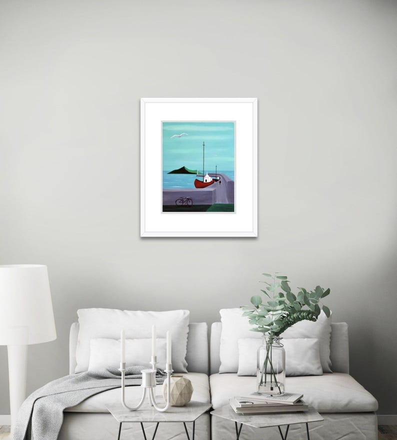 May include: A framed print featuring a painting of a red boat docked at a pier with a bicycle parked nearby. The scene includes a calm blue sea, a distant green island, and a light blue sky with a single white bird flying above the water.